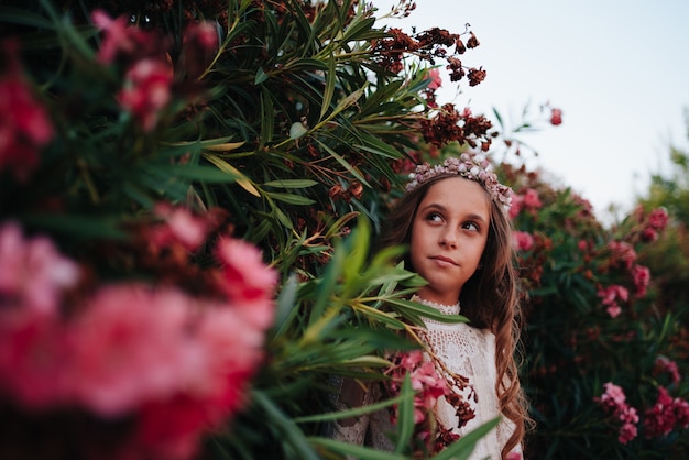 Retrato de uma menina loira com cabelos cacheados, vestida com um vestido de comunhão em um fundo de flores