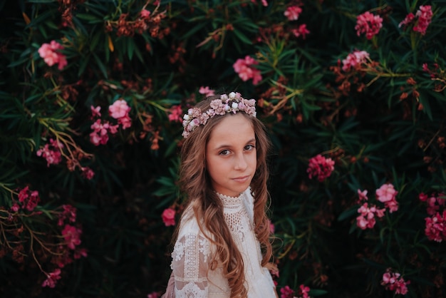 Foto retrato de uma menina loira com cabelos cacheados, vestida com um vestido de comunhão em um fundo de flores