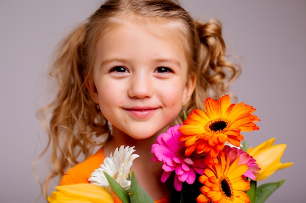 retrato de uma menina loira com um buquê de flores da primavera em uma parede de luz