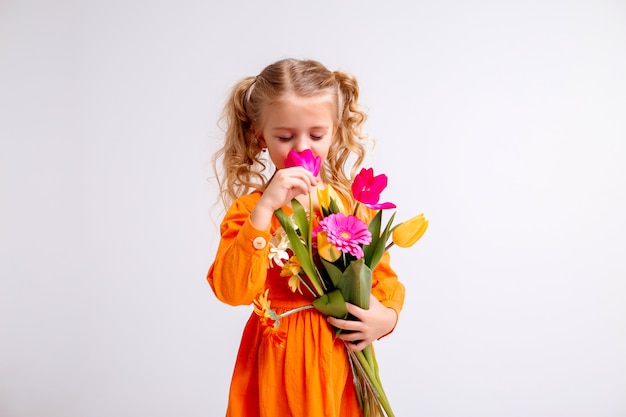 retrato de uma menina loira com um buquê de flores da primavera em uma parede de luz