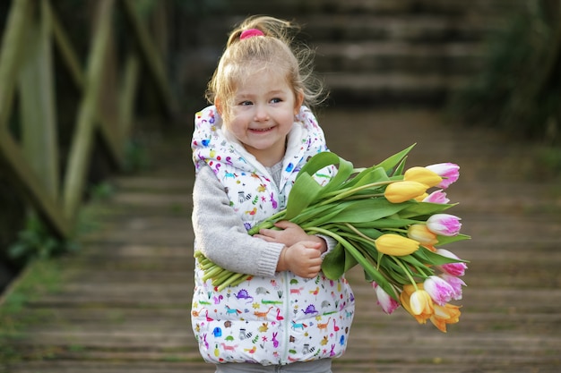 Retrato de uma menina loira com um buquê de tulipas nas mãos