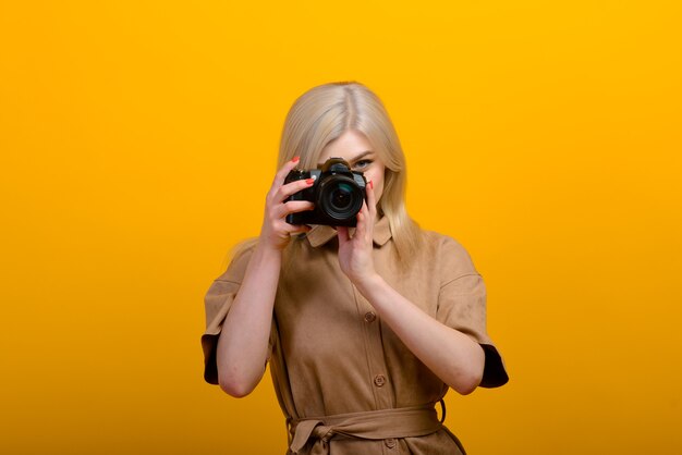 Retrato de uma menina loira com uma câmera na mão em amarelo