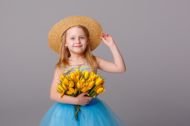 retrato de uma menina loira em um chapéu de palha segurando um buquê de flores da primavera em um espaço em branco