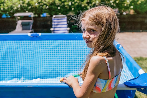 Retrato de uma menina loira enchendo uma piscina removível cottage39s com uma mangueira