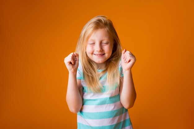 Retrato de uma menina loira feliz em uma camiseta azul em uma parede amarela