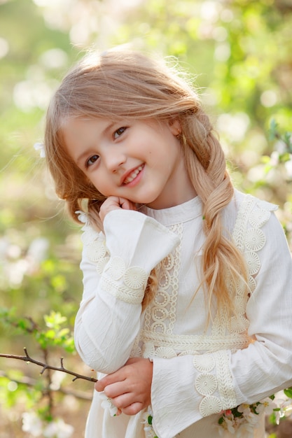 retrato de uma menina loira perto de uma árvore de florescência sorrindo