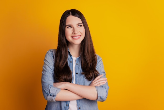 Retrato de uma menina morena curiosa de braços cruzados parece um espaço vazio isolado sobre um fundo amarelo