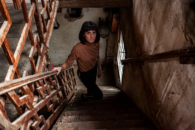 Retrato de uma menina morena na escadaria de uma casa abandonada, imagem com pouca luz