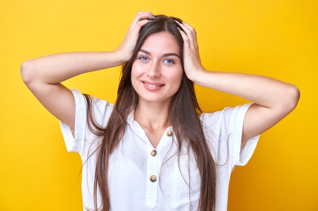 Retrato de uma menina morena segurando a cabeça dela, sorrindo e regozijando-se, isolada no fundo amarelo