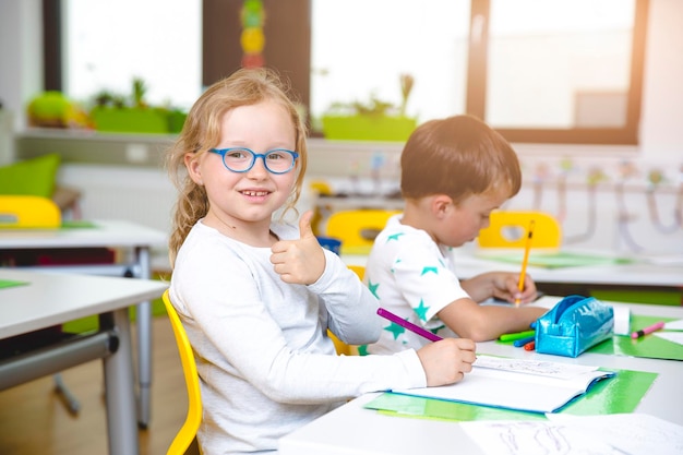 Retrato de uma menina mostrando um sinal de polegar para cima na sala de aula