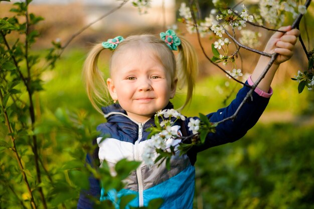 Retrato de uma menina perto de uma cerejeira em flor A criança sorri à luz do sol