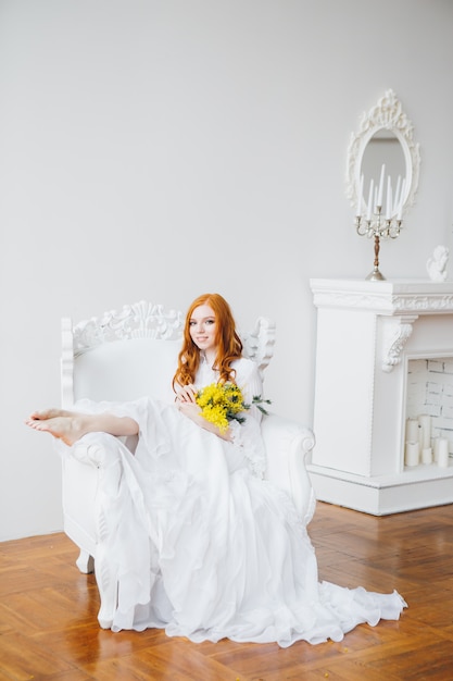 Retrato de uma menina ruiva linda com uma Mimosa em um vestido longo branco