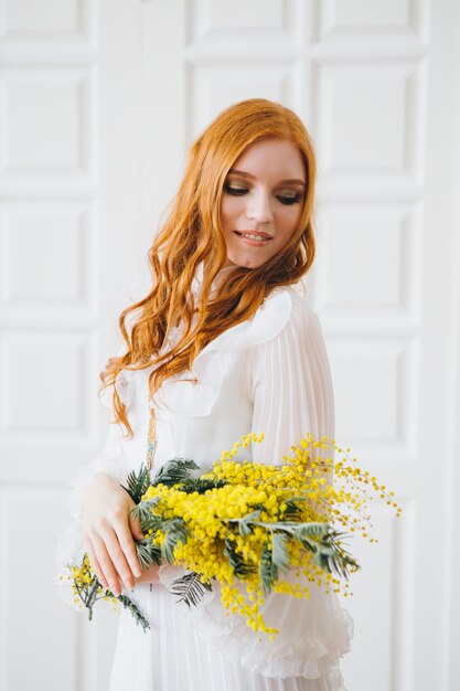 Retrato de uma menina ruiva linda com uma Mimosa em um vestido longo branco