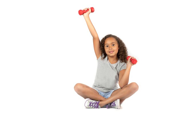 Foto retrato de uma menina se exercitando com halteres enquanto está sentada contra um fundo branco