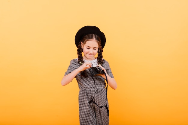 Retrato de uma menina segurando uma câmera fotográfica isolada em um fundo amarelo