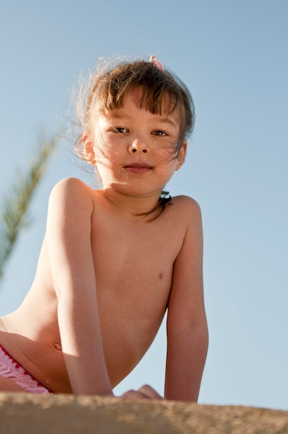 Retrato de uma menina sem camisa sentada na areia contra um céu claro