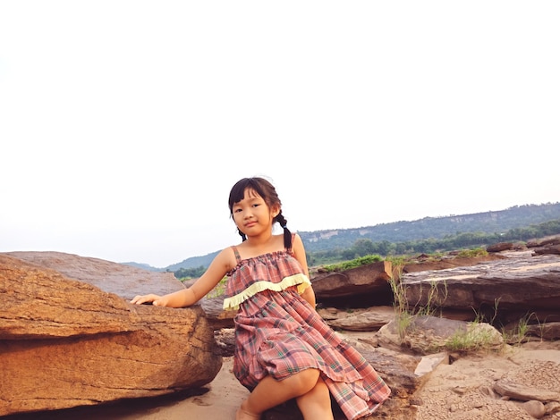 Foto retrato de uma menina sentada em rochas contra um céu claro