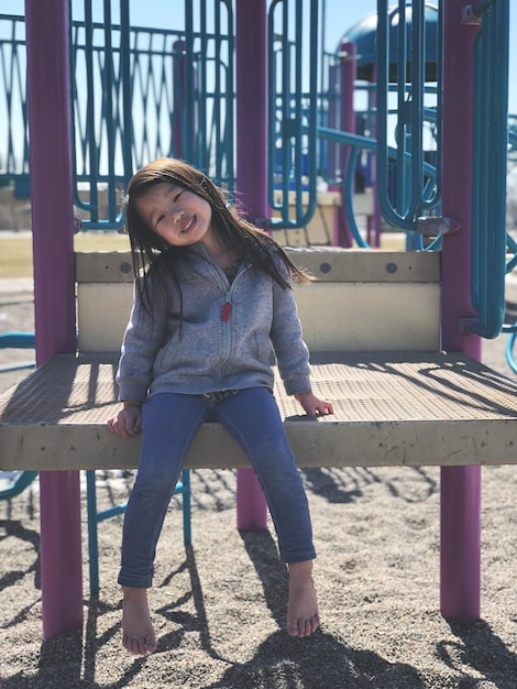 Retrato de uma menina sentada em um equipamento de brincadeira no playground