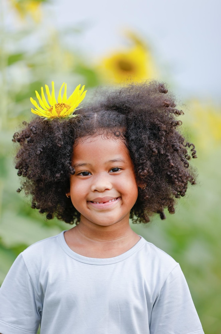Foto retrato de uma menina sorridente com cabelos encaracolados e uma flor