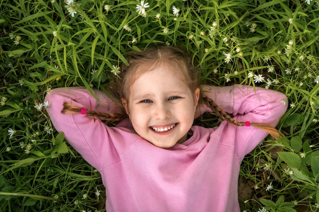 Retrato de uma menina sorridente com tranças, deitado sobre um prado de flores.