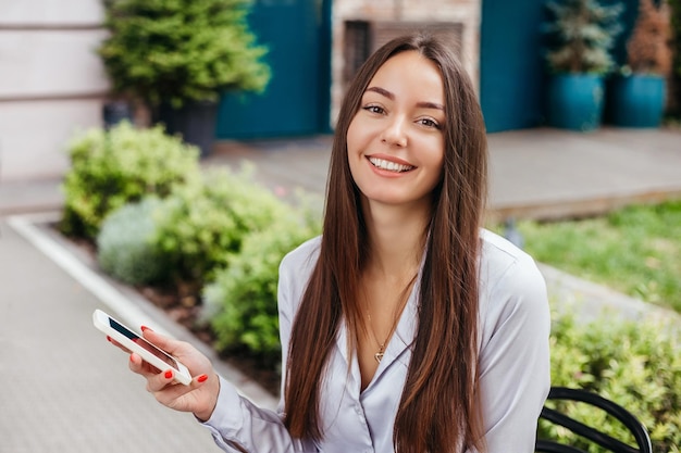 Retrato de uma menina sorridente com um telefone celular no contexto da fachada do café