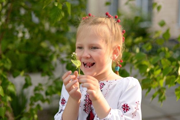 Retrato de uma menina sorridente com uma flor em uma camisa bordada ucraniana As emoções da criança de feliz