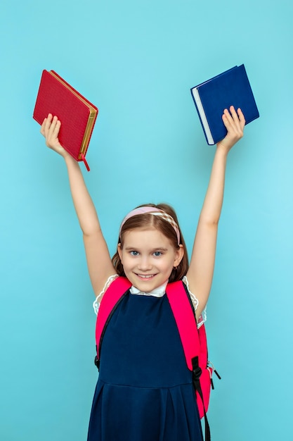 Retrato de uma menina sorridente com uma mochila e livros, mãos levantadas