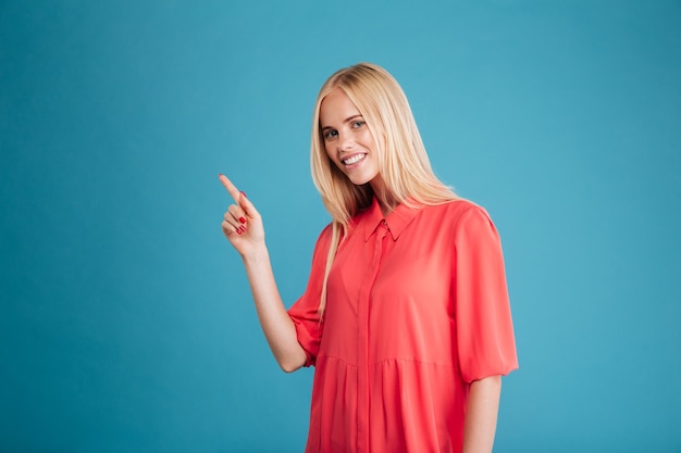 Retrato de uma menina sorridente com vestido vermelho apontando o dedo isolado em uma parede azul