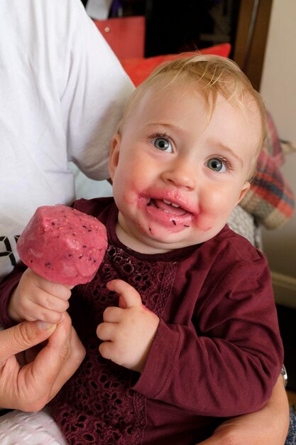 Foto retrato de uma menina sorridente comendo sorvete enquanto está sentada com a mãe em casa