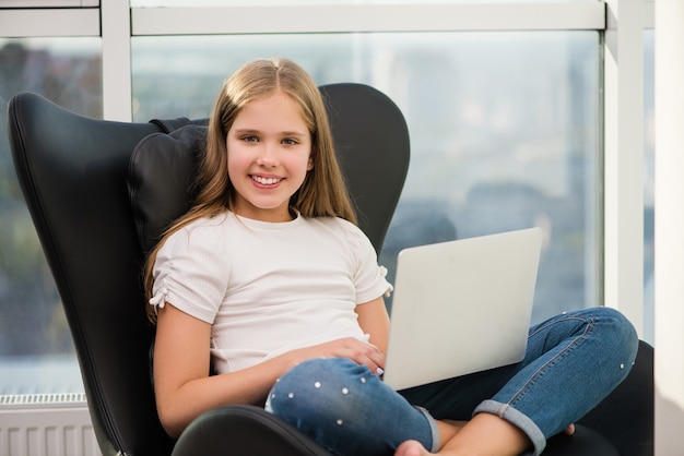 Retrato de uma menina sorridente da escola sentada com um laptop