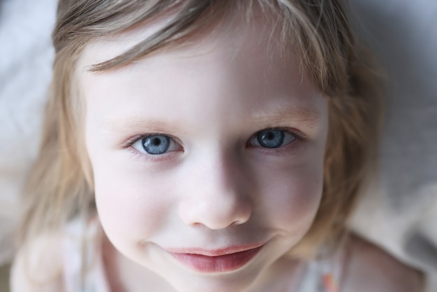 Retrato de uma menina sorridente de olhos azuis na cama