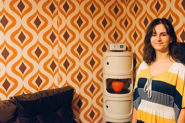 Foto retrato de uma menina sorridente de pé junto à parede em casa