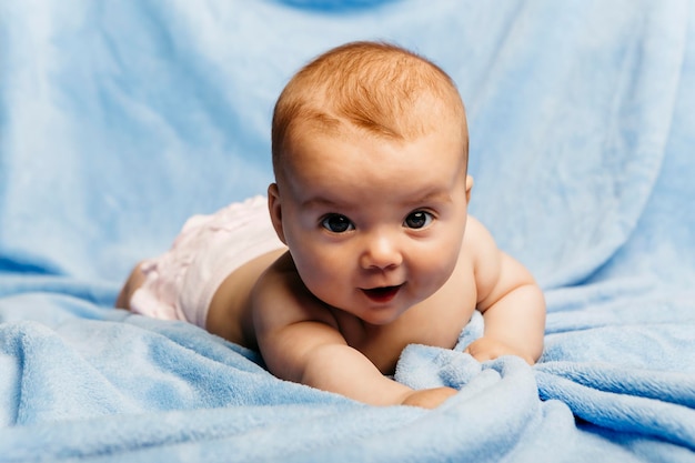 Retrato de uma menina sorridente deitada no cobertor azul claro