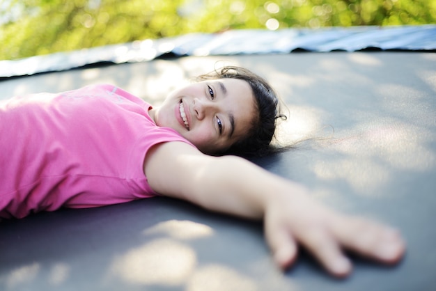 Retrato de uma menina sorridente deitada no trampolim