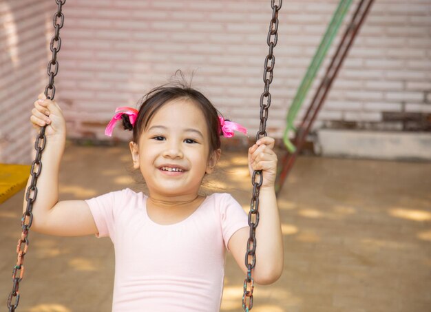 Foto retrato de uma menina sorridente em um baloiço no playground