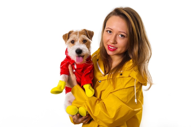 Retrato de uma menina sorridente em uma capa de chuva amarela com um cachorro Jack Russell Terrier em uma jaqueta vermelha nos braços. Isolado em fundo branco