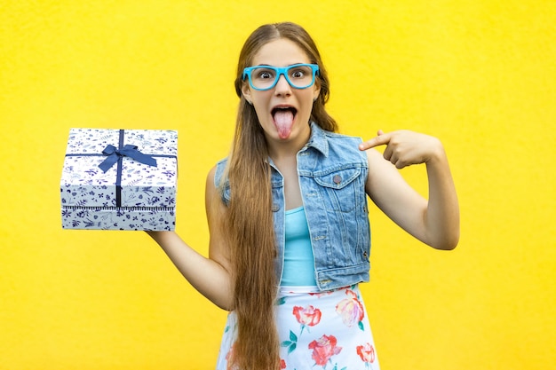 Retrato de uma menina sorridente, hippie feliz com vestido e óculos azuis, segurando uma caixa de presente e dentuça