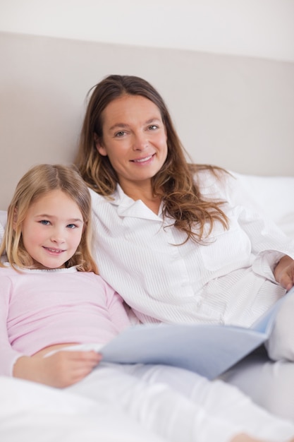 Retrato de uma menina sorridente lendo um livro com sua mãe