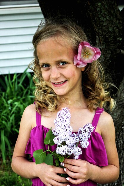 Retrato de uma menina sorridente segurando flores enquanto está de pé contra as plantas