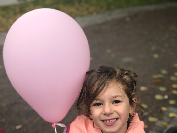Foto retrato de uma menina sorridente segurando um balão rosa enquanto está de pé na estrada