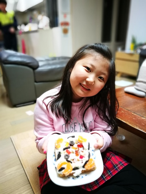 Foto retrato de uma menina sorridente segurando um prato com comida em casa