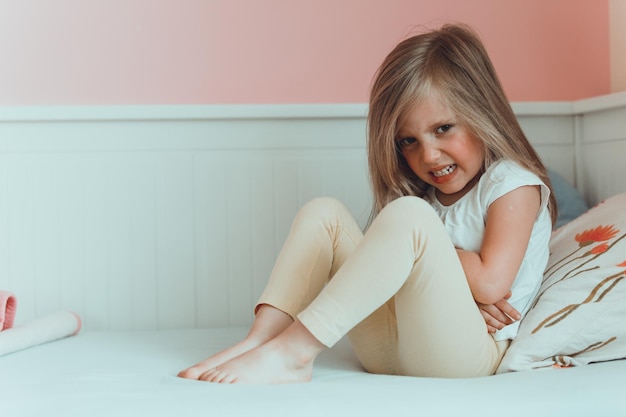 Retrato de uma menina sorridente sentada na cama em casa.