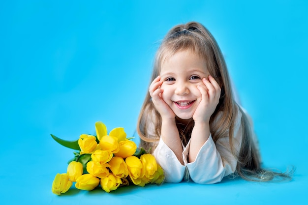 Retrato de uma menina sorridente uma criança com um buquê de tulipas amarelas em um fundo azul isolado Estilo de vida Internacional da Mulher ou Dia das Mães Espaço para texto Fotografia de alta qualidade