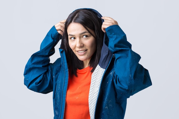 Retrato de uma menina sorridente, vestida com capa de chuva azul em gotas posando com capuz em cinza