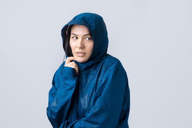 Retrato de uma menina sorridente, vestida com capa de chuva azul em gotas posando com capuz em cinza