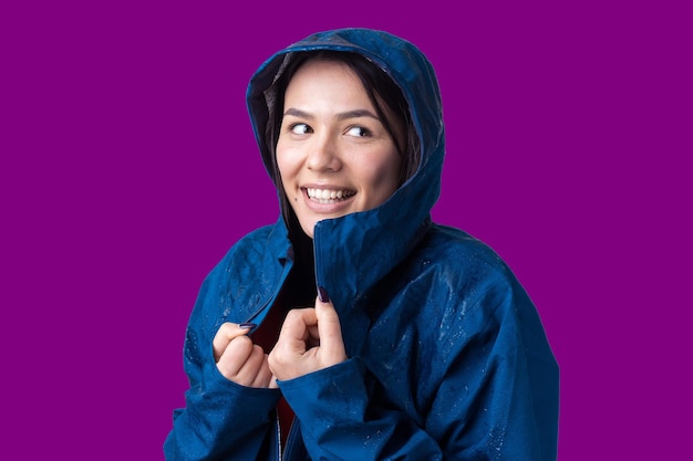 Foto retrato de uma menina sorridente vestida com capa de chuva azul em gotas posando com capuz em fundo cinza em um estúdio