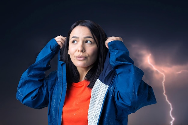 Retrato de uma menina sorridente, vestida com capa de chuva azul em gotas posando com capuz no contexto de um céu sombrio com relâmpagos.