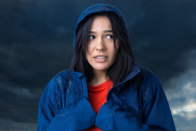 Retrato de uma menina sorridente, vestida com uma capa de chuva azul e pingentes posando com capuz