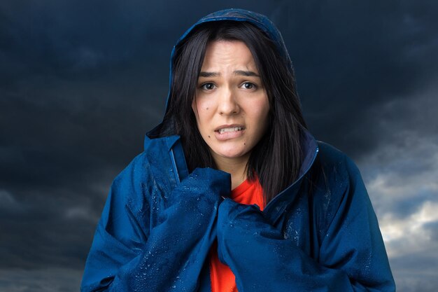 Retrato de uma menina sorridente, vestida com uma capa de chuva azul e pingentes posando com capuz