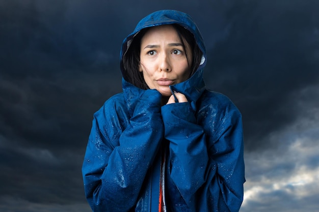 Retrato de uma menina sorridente, vestida com uma capa de chuva azul e pingentes posando com capuz